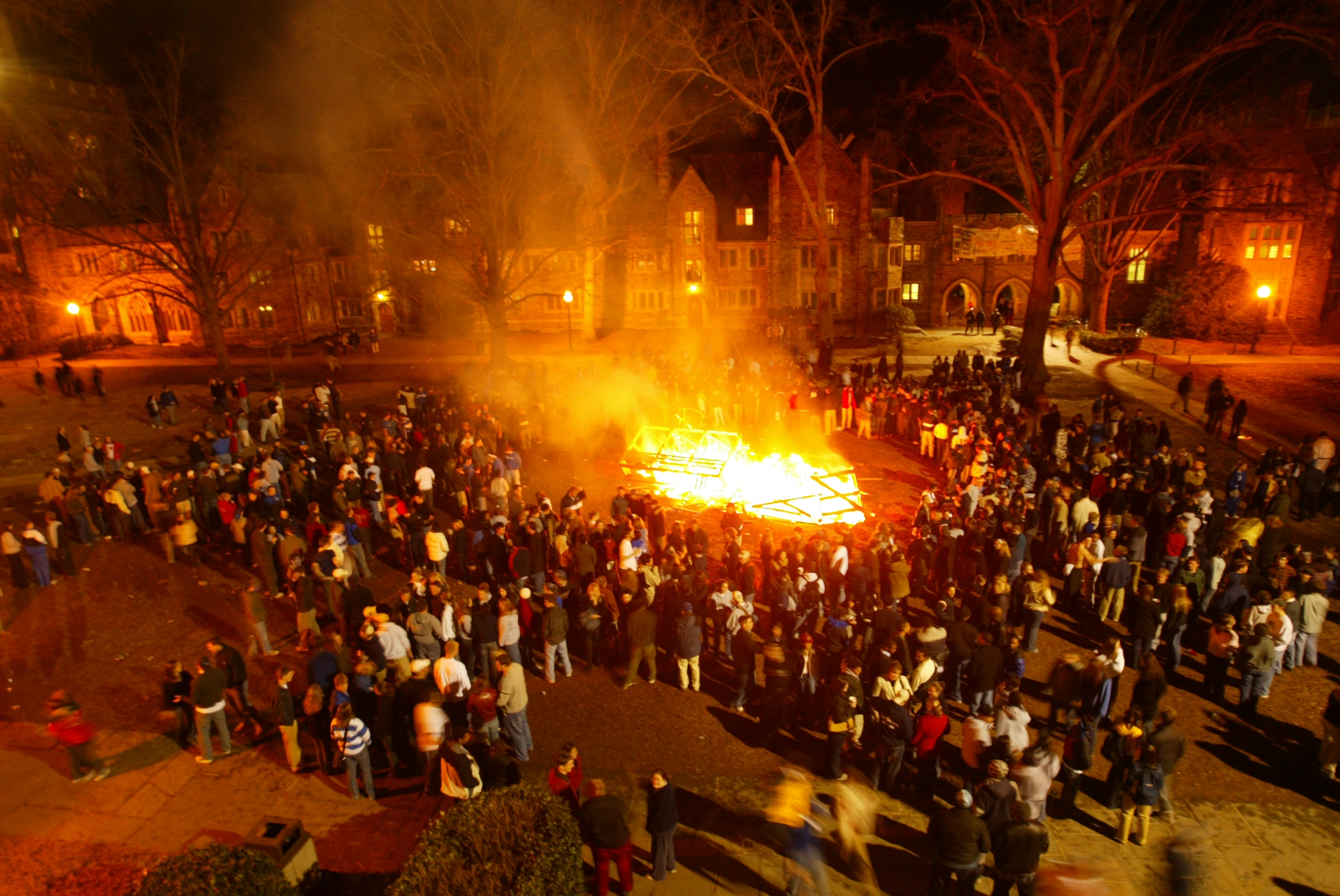 A crowd gathers around a large bonfire in the middle of a quad at Duke University