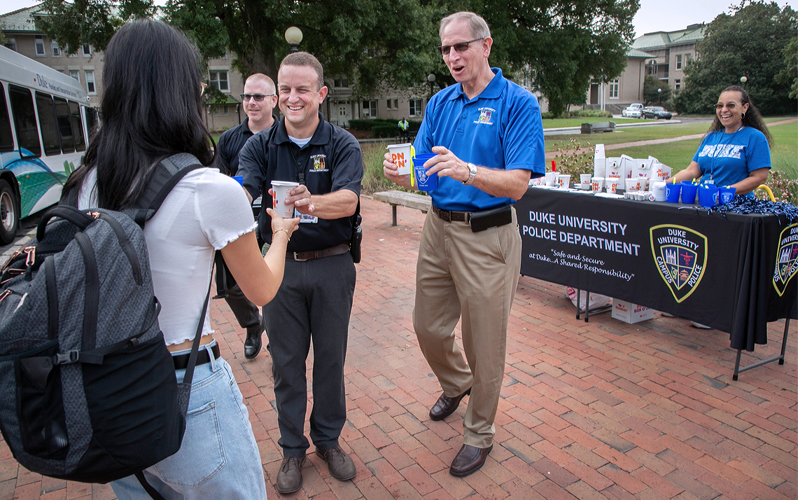 Two Duke Police officers hand out coffee and doughnuts to a student wearing a backpack.