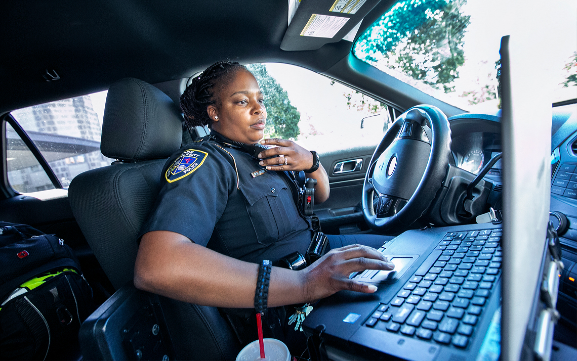 A female police officer looks at her computer while sitting in her police cruiser