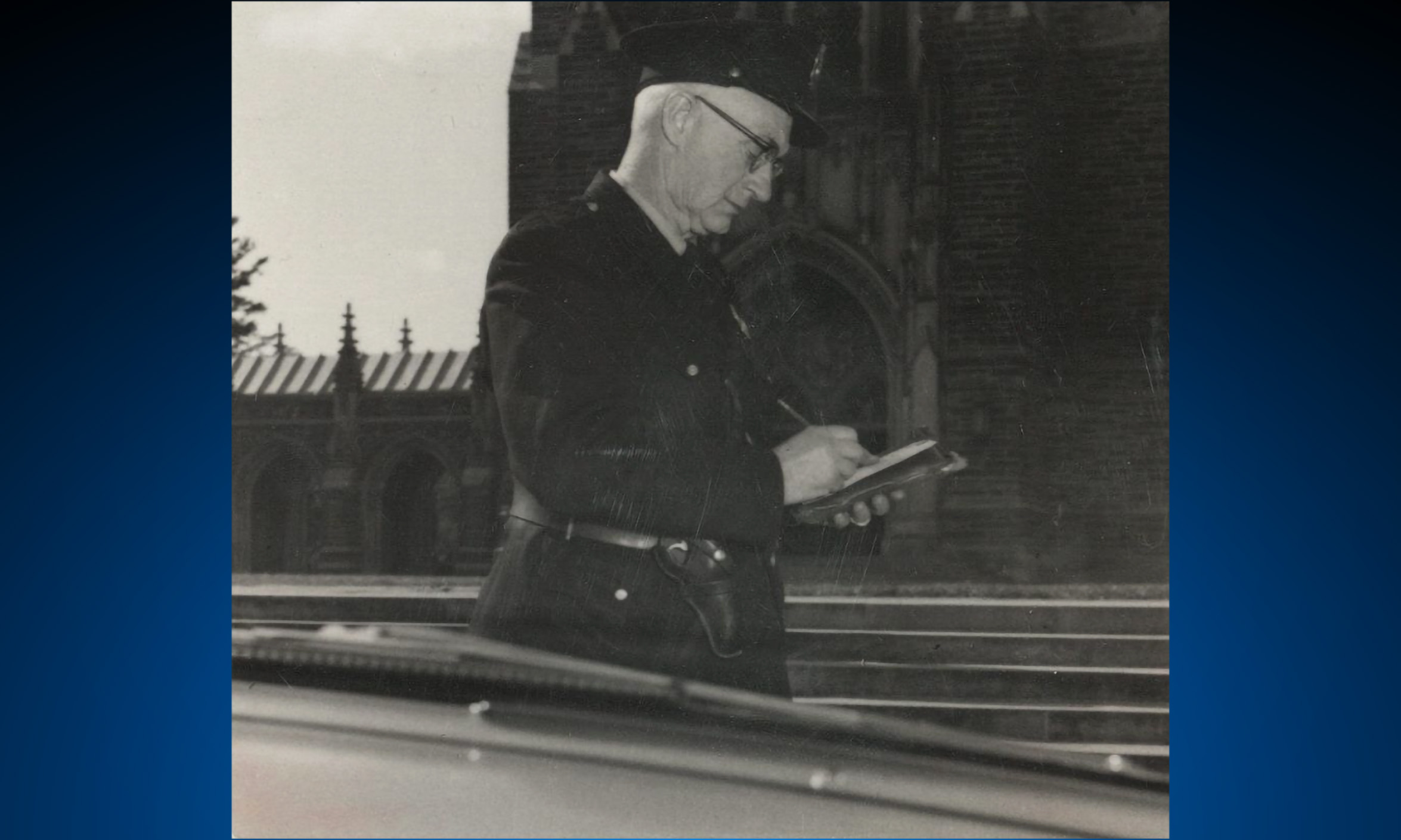 A Duke Police officer writes a ticket while standing outside a gothic building.