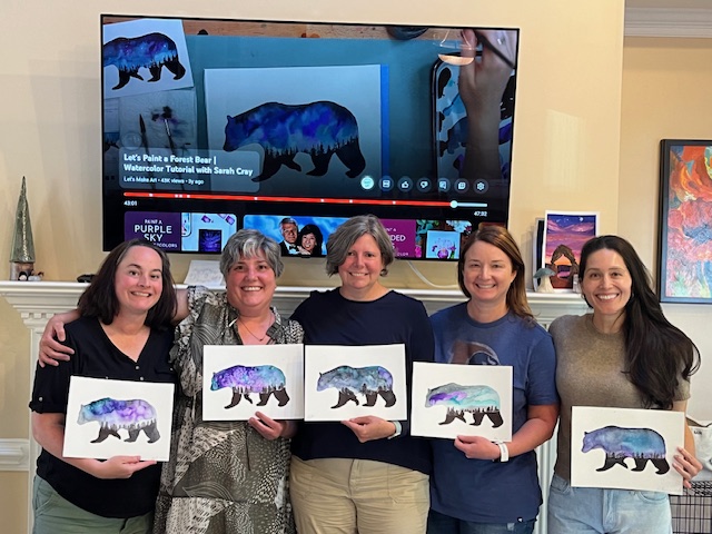 five women hold paintings of a bear