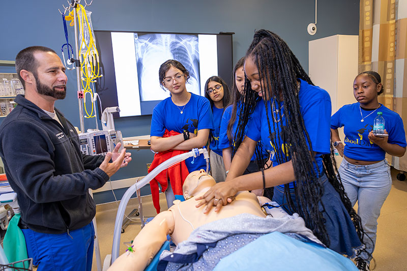 Students practice CPR on a dummy while an instructor helps