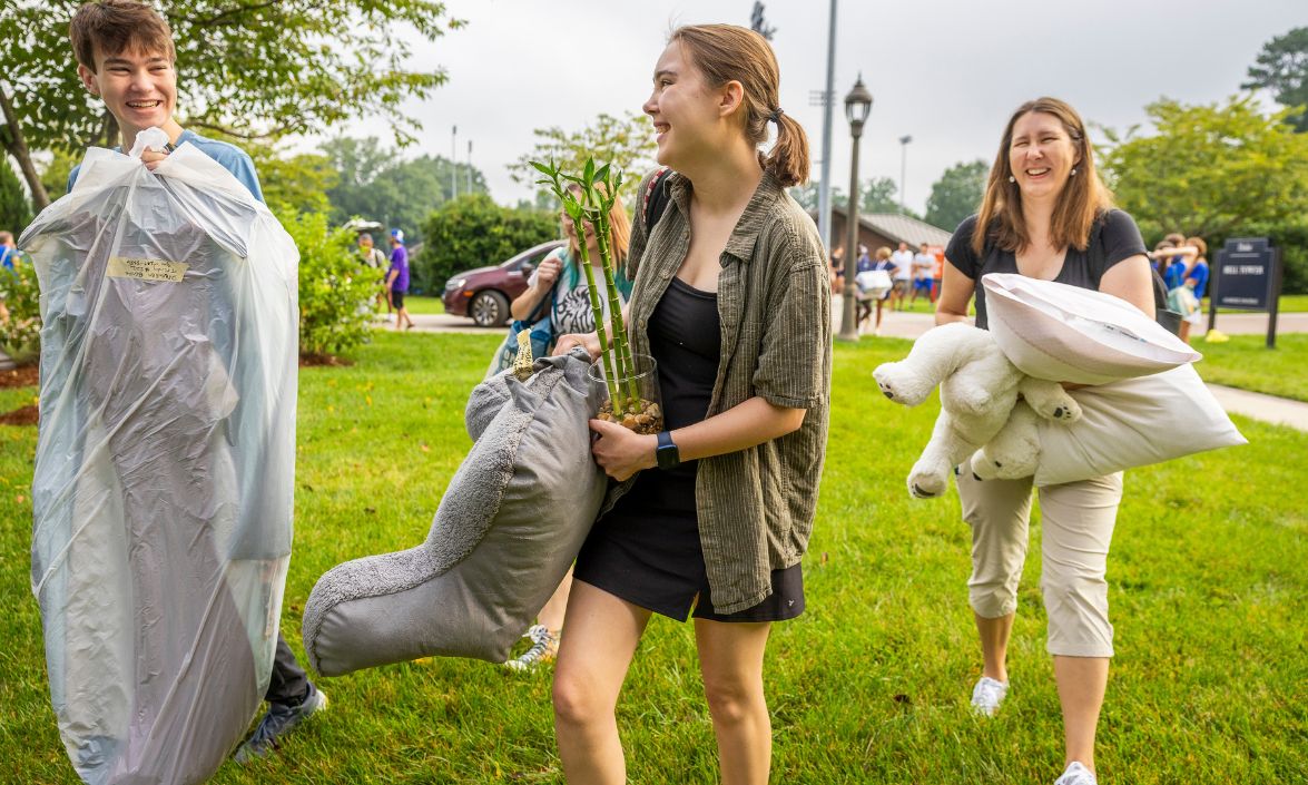 Person carrying bedding with two people, laughing.