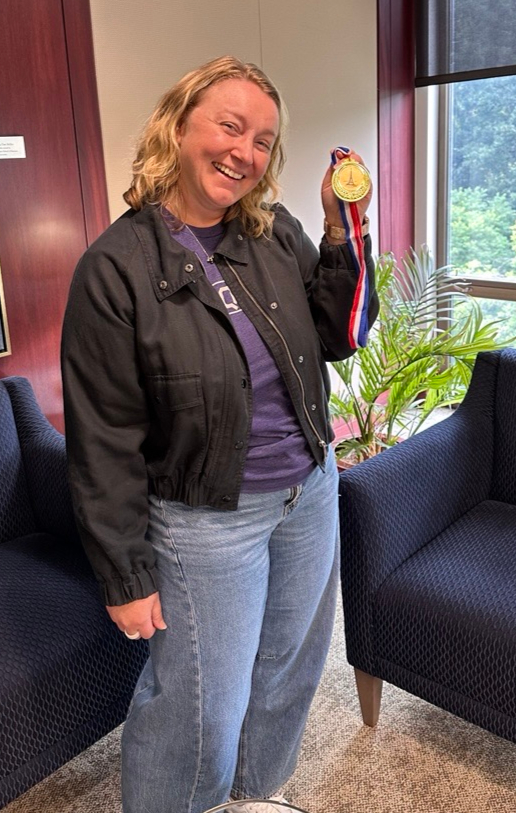 A woman smiles while holding a medal