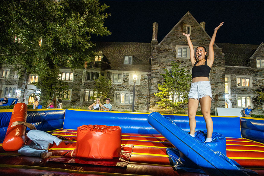 A student celebrates knocking another student off a perch with a foam block at a carnival game