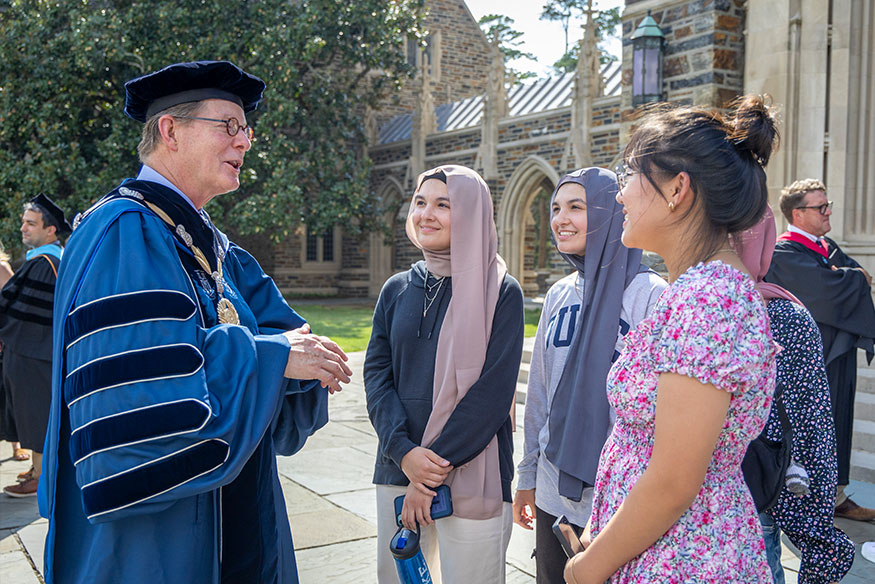 President Price in academic robes talking with students outside of Duke Chapel