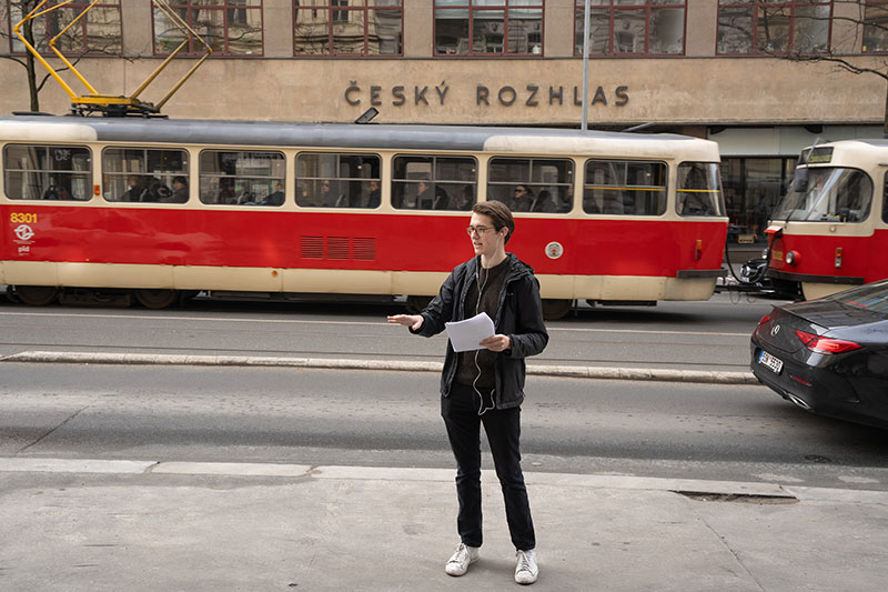 Another student give their talk on a city street as an old red-striped street car passes