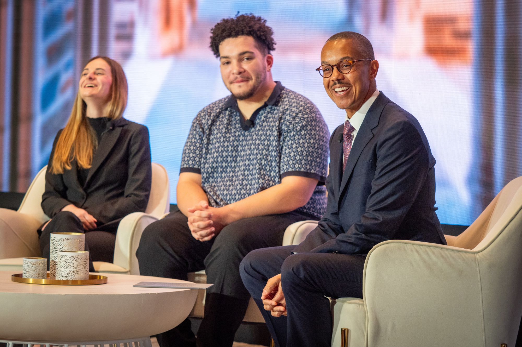 Three people sit on chairs on a stage, laughing at a comment from the audience.
