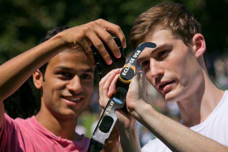 Vinay Kshirsagar and Xavier Boudreau use eclipse glasses to cover the lens of a iPhone while taking a video. Photo by Megan Mendenhall