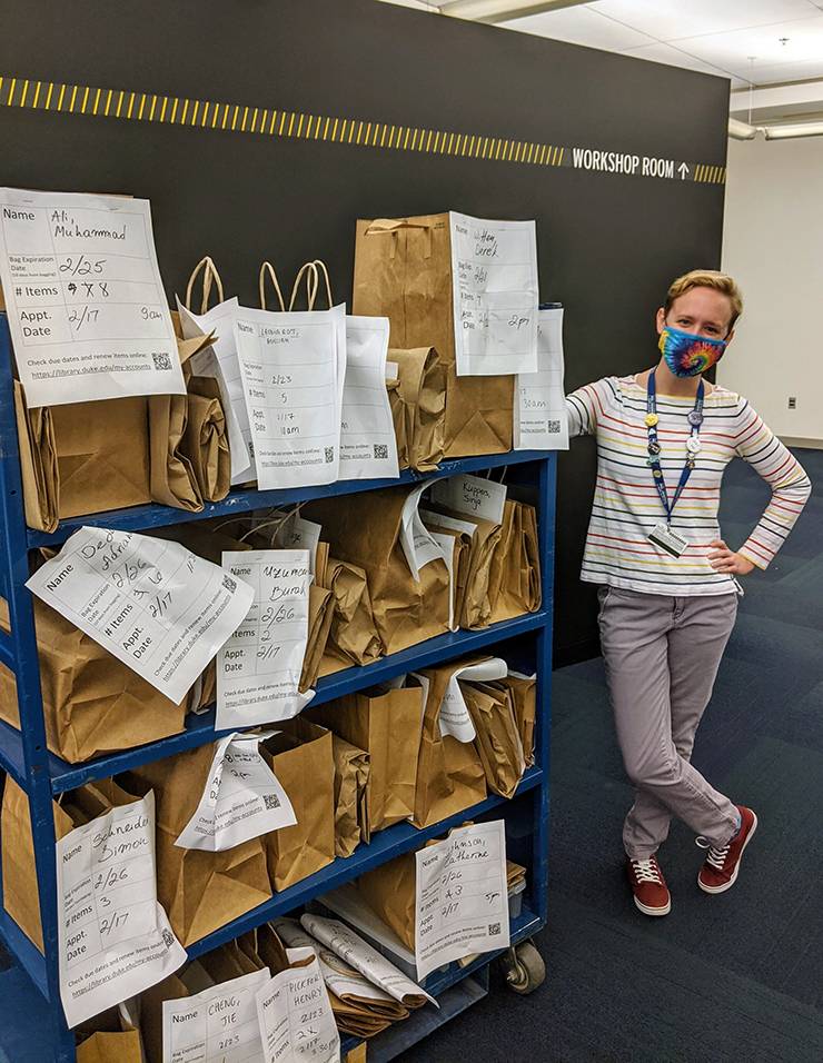 Access and Library Services Coordinator Kelli Stephenson stands next to a cart of books that are ready for Library Takeout. Photo courtesy of Kelli Stephenson.