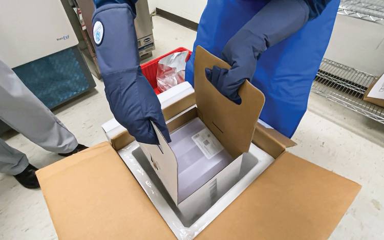 Jordan DeAngelis lifts Duke’s first allotment of Pfizer/BioNTech COVID-19 vaccines out of a cardboard box with dry ice. Photo  by Shawn Rocco.