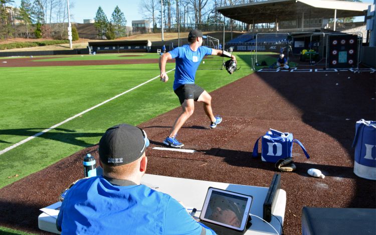 Duke Baseball Graduate Manager Coleman Williams, left, tracks real-time pitch data from pitcher Adam Boucher during practice. Photo by Stephen Schramm. 