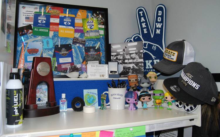 Devin Demyanovich has a shelf filled with mementos from some of the events athletes she works with have qualified for. Photo by Stephen Schramm.