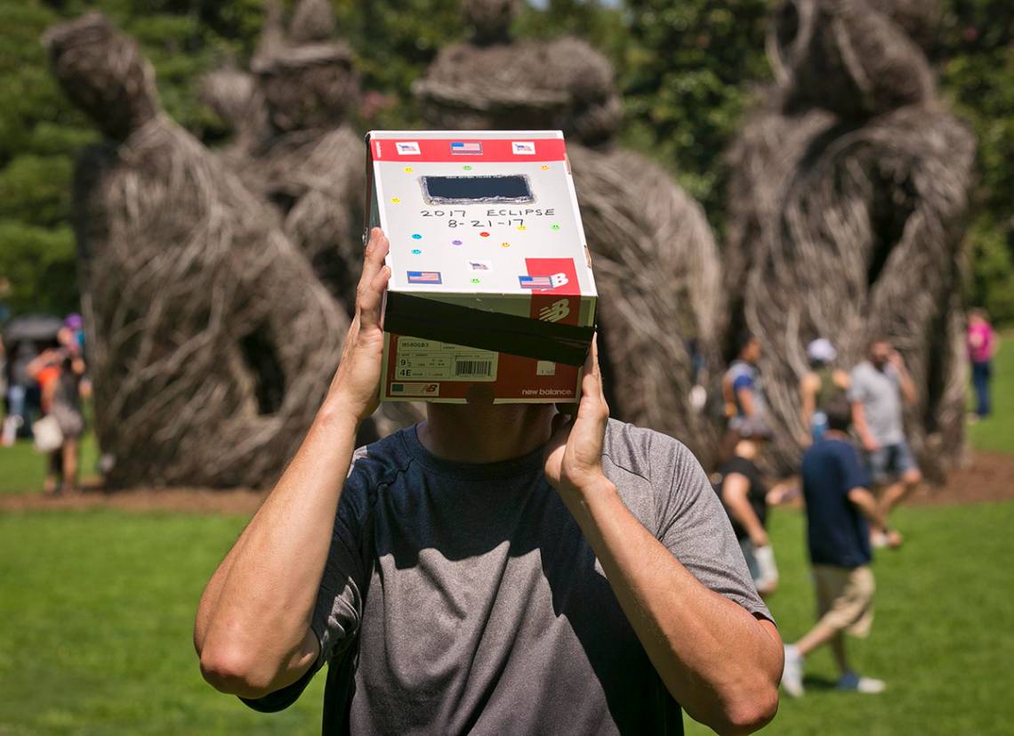 Wayne Little uses a homemade device made of welders glass and a cardboard box to watch the eclipse in Duke Gardens. Photo by Megan Mendenhall/Duke Photography