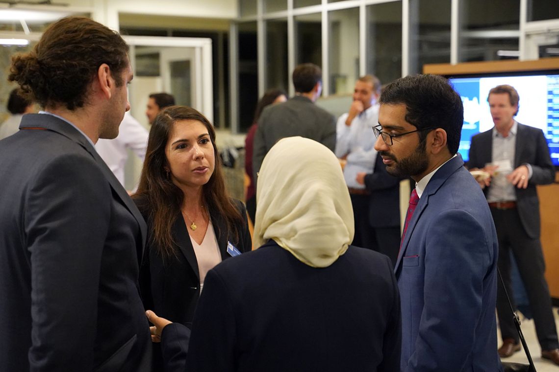 Four individuals in business attire speak in a huddle at a conference.