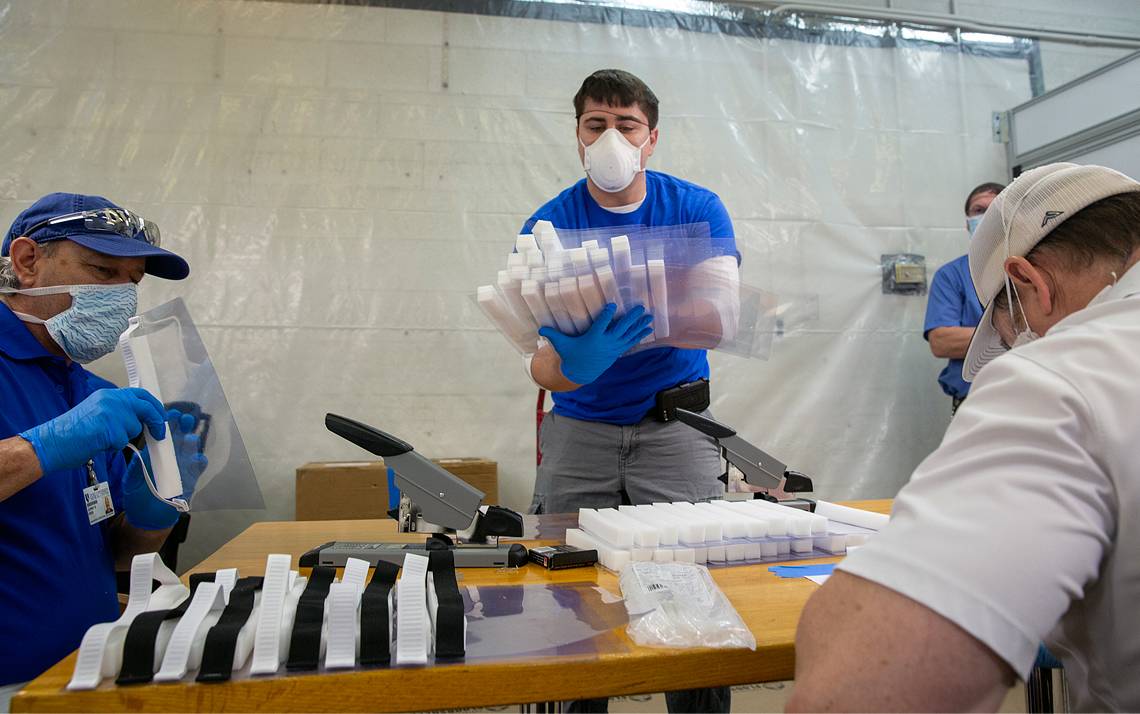 Three people assemble face shields.