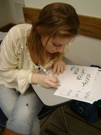 A student writes out an Arabic phrase.