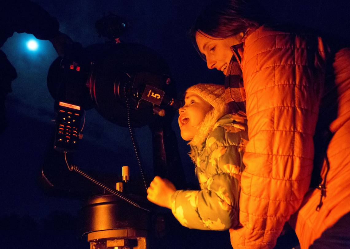 Maura Farver of Durham holds Poppy Overman, 3, in awe as she views the moon's craters through a telescope at the Duke Teaching Observatory in Duke Forest. Photo by Jared Lazarus, Duke University.