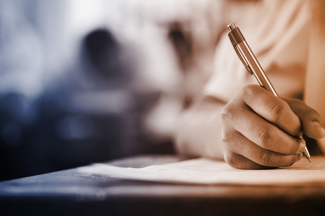 image of student writing at a classroom desk