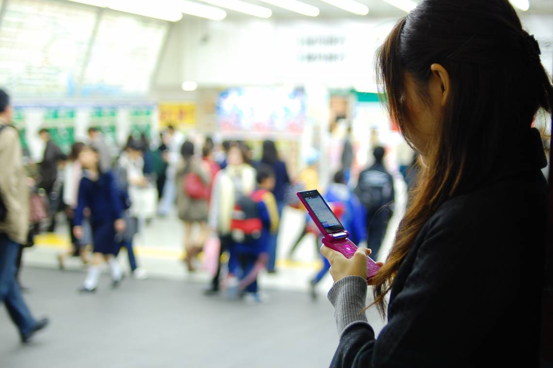 Girl consults her cell phone screen in a crowded subway station