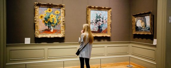 A woman stood looking at a painting of flowers at an art museum