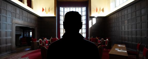 A persons silhouette in front of the conference table and dark wood walled room of Berlin’s Cecilienhof Country House