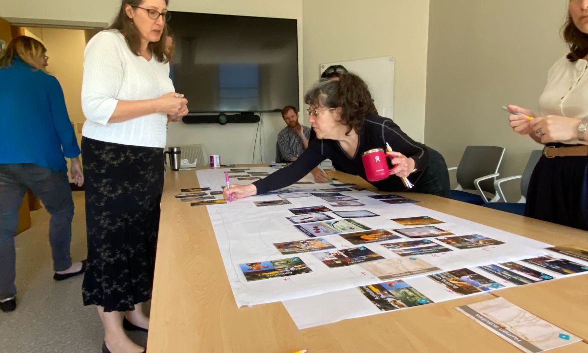 Instructors stand around table with a maps and images across it.