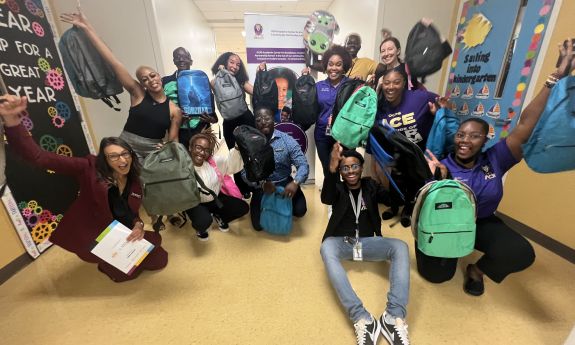Group of students in a school hallway holding up backpacks.