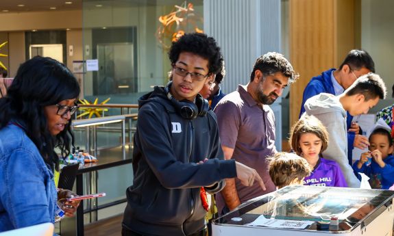 Community members learning about laser engraving and 3-d printing as one of the sponsors, Duke’s Innovation Co-Lab led these workstations and gave out fidget 3d prints and Duke Centennial tags. Photo by John Shockey