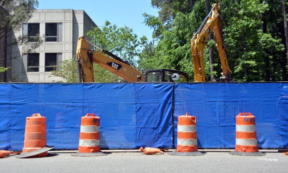 Utility work takes place behind a blue fence.