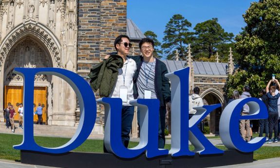 Two duke alumni stand behind large Duke lettering near Duke Chapel