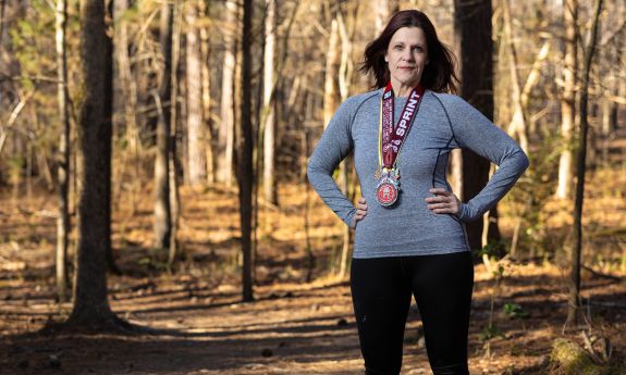A portrait of Rachel Orr, as she stands in a wooded area wearing race medals