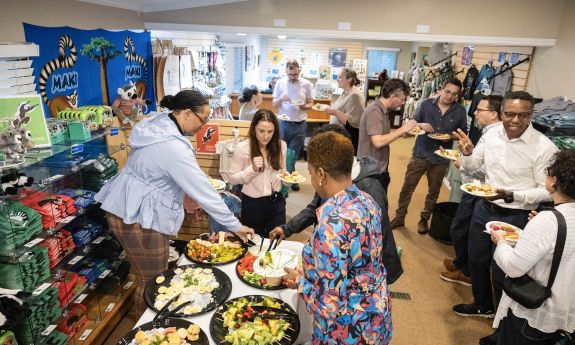 A group of people gather in the Duke Lemur Center's visitor center, talking and surrounding a table of appetizers