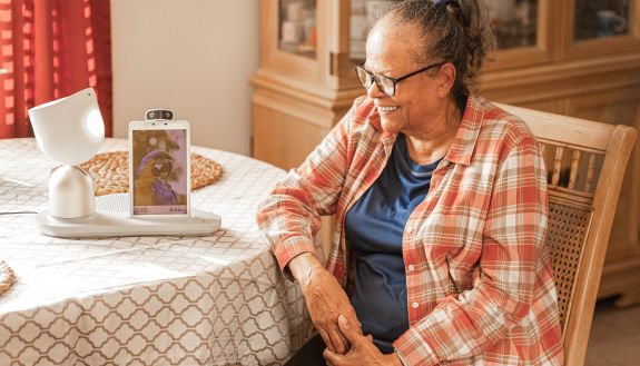 A smiling woman looks at a companion robot that's displaying a picture of a macaw