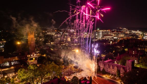 An aerial view of fireworks bursting over West Campus with Duke Chapel and Duke Hospital in the background