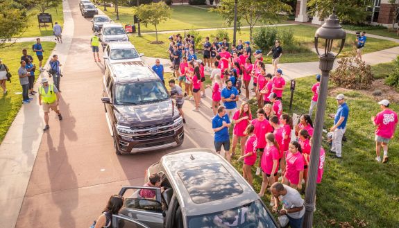 aerial photo of line of vans on East Campus while President Price and students prepare to help students move in.