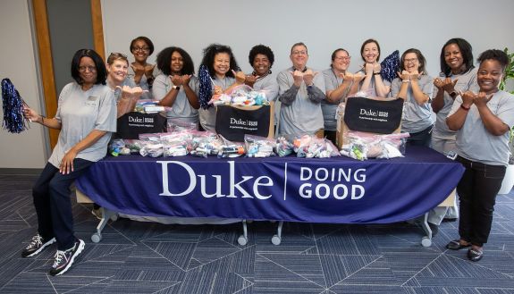 Staff gathered around a table that has a "Duke Doing Good" banner.