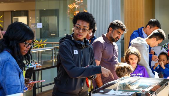 Community members learning about laser engraving and 3-d printing as one of the sponsors, Duke’s Innovation Co-Lab led these workstations and gave out fidget 3d prints and Duke Centennial tags. Photo by John Shockey