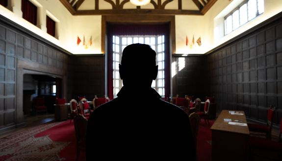 A persons silhouette in front of the conference table and dark wood walled room of Berlin’s Cecilienhof Country House