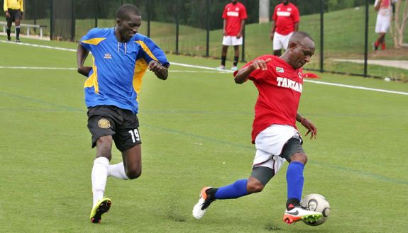 Two people playing soccer, one is Charles Muiruri on the right wearing a red shirt that says Tanzania on it