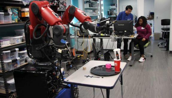 Red robot in a lab with two people in the background