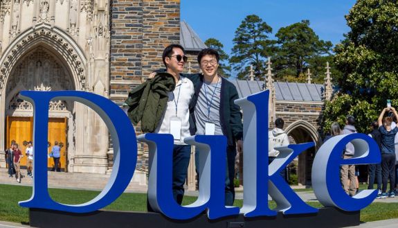 Two duke alumni stand behind large Duke lettering near Duke Chapel