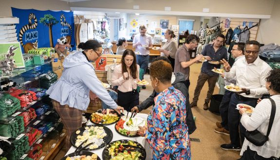 A group of people gather in the Duke Lemur Center's visitor center, talking and surrounding a table of appetizers