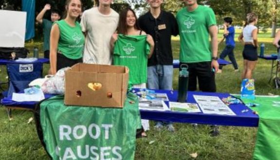 Group of people outside behind a table that says "root causes"