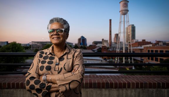Mayme Webb-Bledsoe poses with her arms folded in front of Durham's iconic Lucky Strike tower.