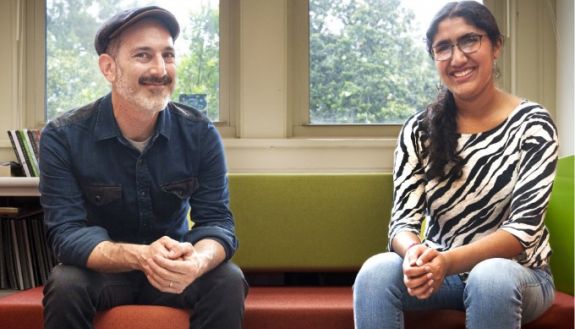 Two people sitting on a couch looking at the camera and smiling