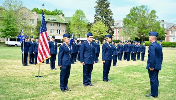 Group of students in military uniform standing on the grass with a flag