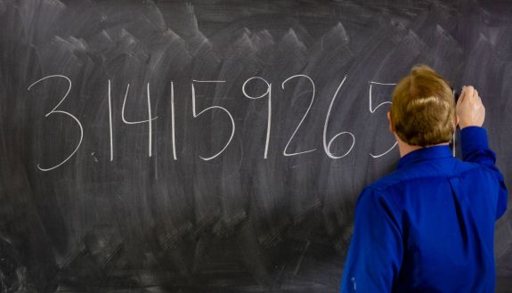 A math professor writes out pi on a chalkboard.