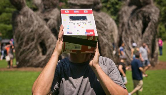 Wayne Little uses a homemade device made of welders glass and a cardboard box to watch the eclipse in Duke Gardens. Photo by Megan Mendenhall/Duke Photography