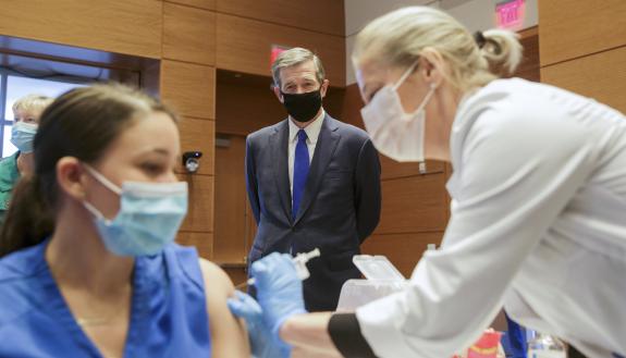 Governor Roy Cooper watches as a Duke Health employee receives their vaccination